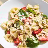 Frische Bow-Tie-Pasta mit Babyspinat, Erdbeerscheiben und einer cremigen Mohnsamen-Dressing auf einem rustikalen Teller.  