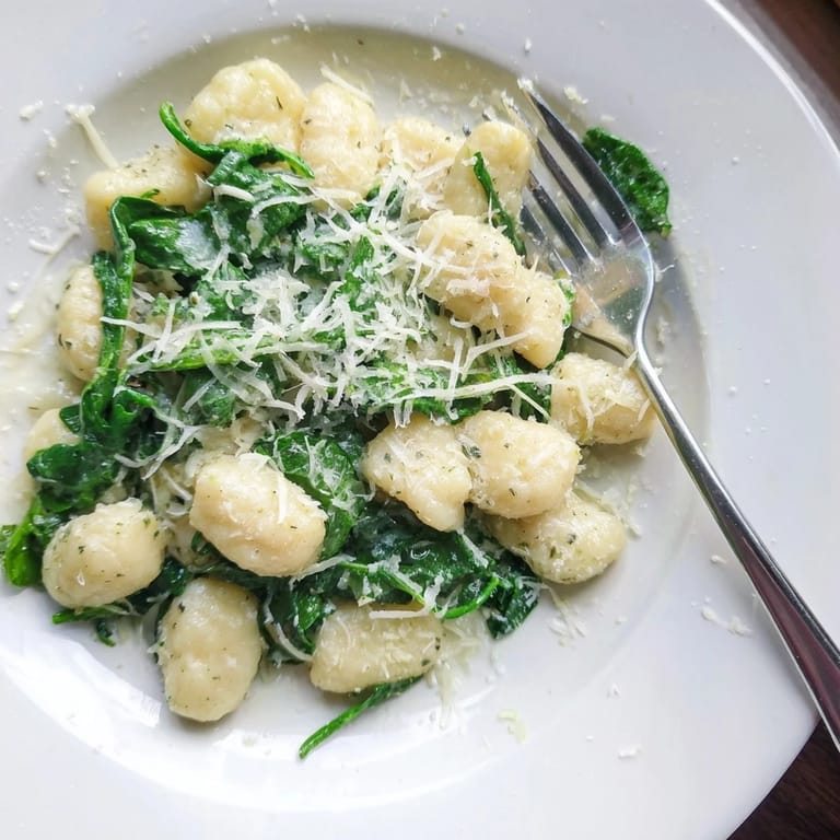 Potato gnocchi with fresh spinach coated in a fragrant creamy garlic sauce, topped with black pepper and Parmesan for a cozy Italian-inspired dinner.